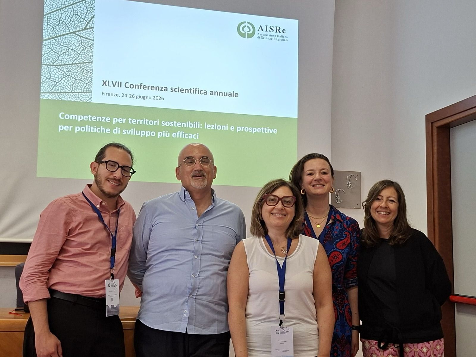 Cinque partecipanti posano davanti alla schermata della XLVII Conferenza scientifica annuale AISRe.