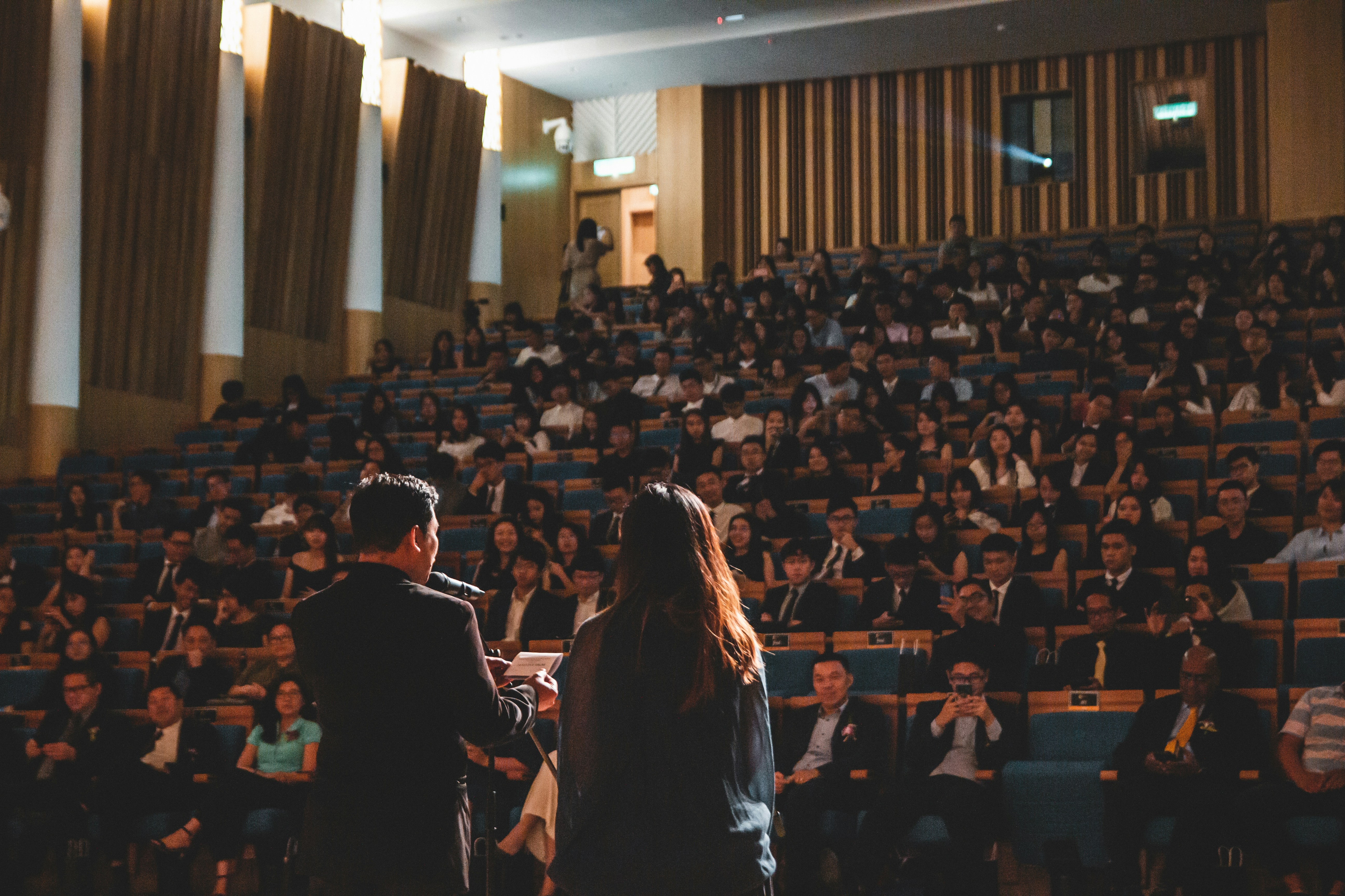 Due relatori sul palco si rivolgono a un ampio pubblico in un auditorium affollato.